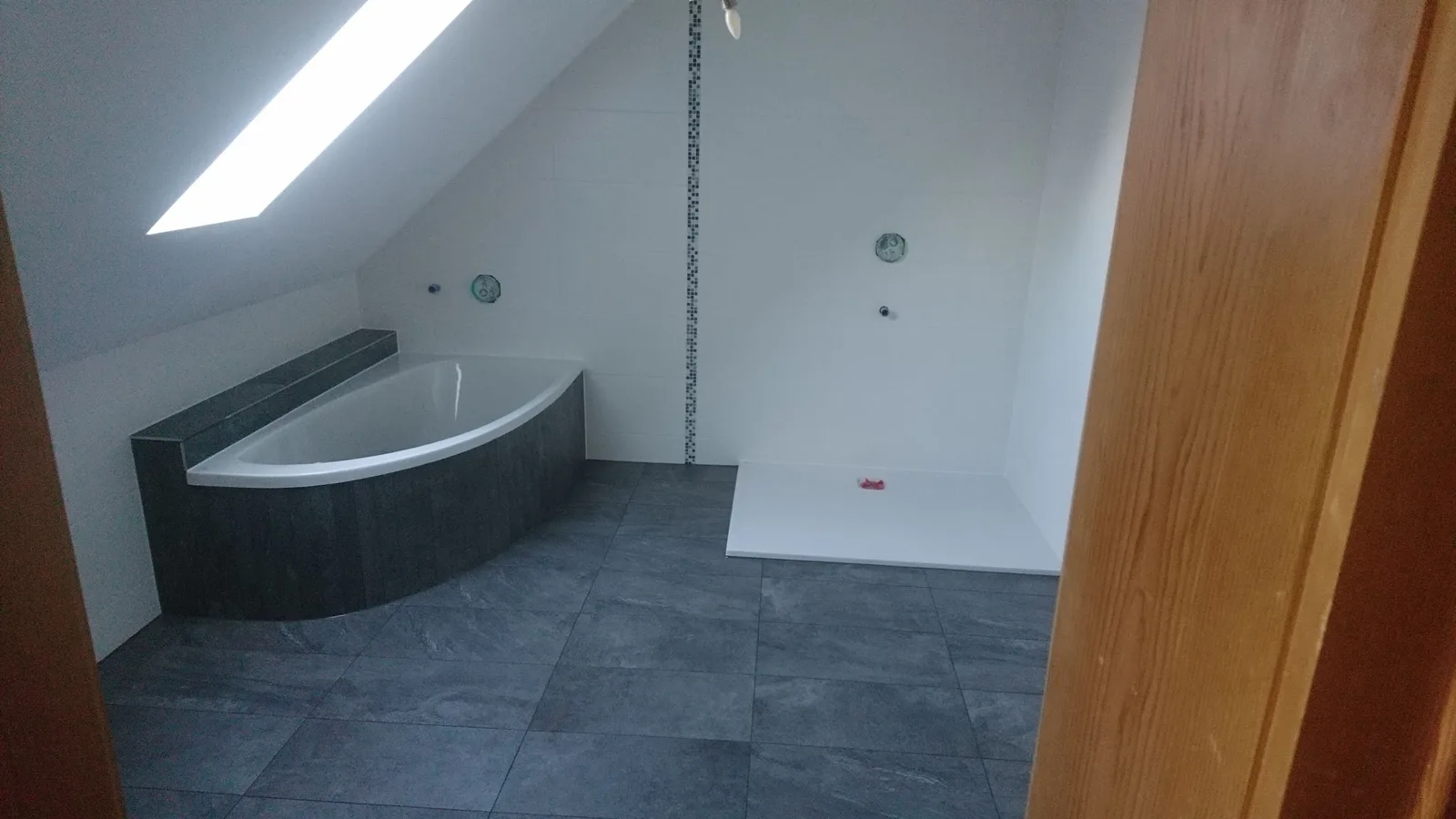 Bad unter einer Dachschräge mit dunklem Fliesenboden und verfliester Eckbadewanne
