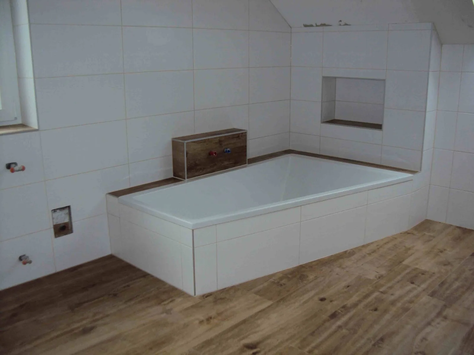 Bad mit weiß verfliester Badewanne, Wandnische und Boden in Holzoptik