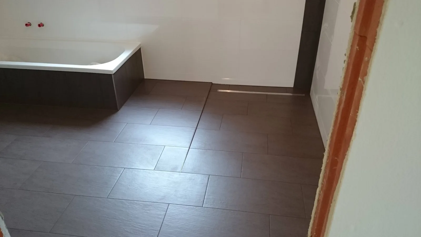 Bad mit dunklem Fliesenboden, verfliester Badewanne und Duschrinne